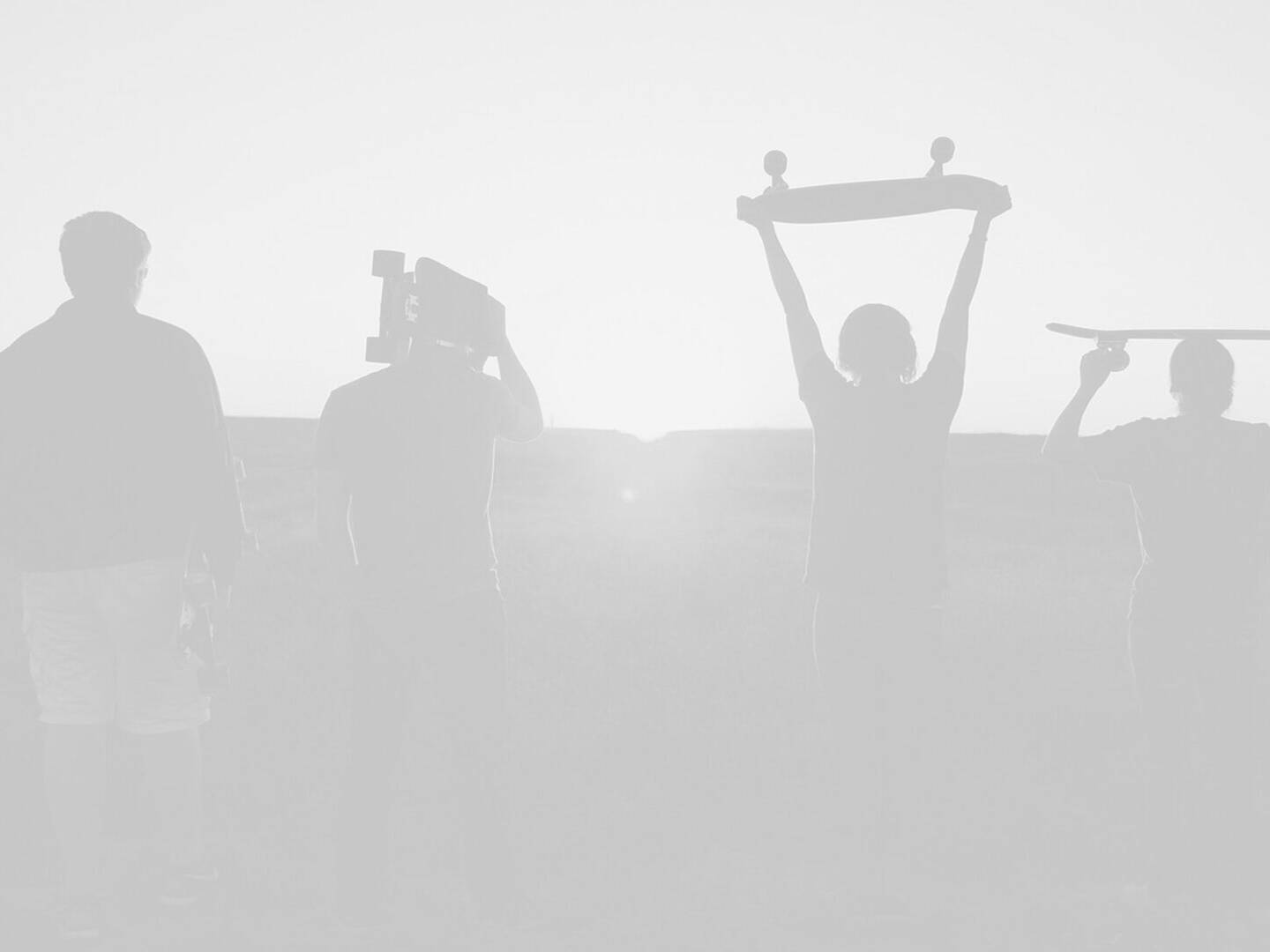 Silhouette of a group of people holding skateboards.