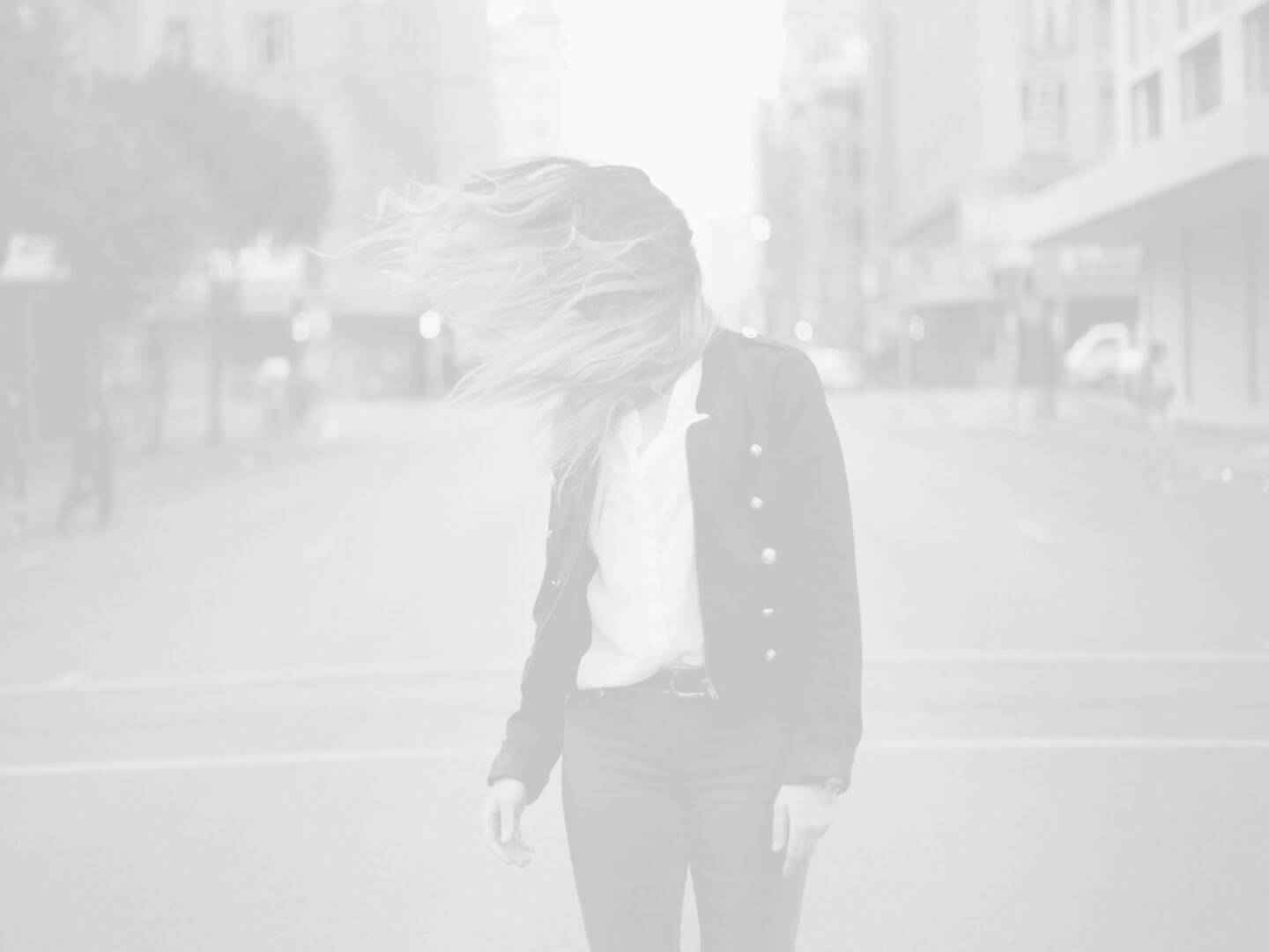 A woman walking down the street with her hair blowing in the wind.