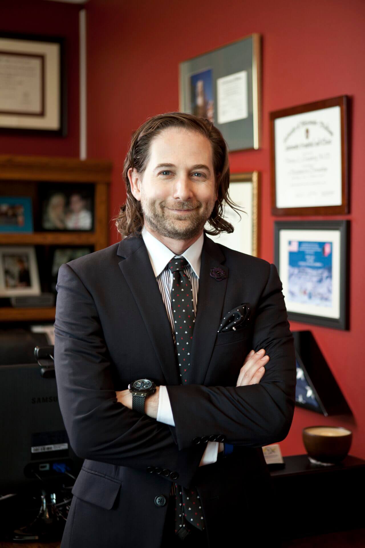 Man in suit, arms crossed, office background.